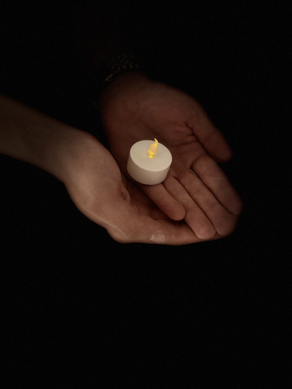 Two open hands holding a small glowing candle